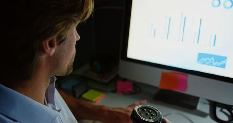 Young Male Executive Analyzing Data on Computer Screen Drinking Coffee