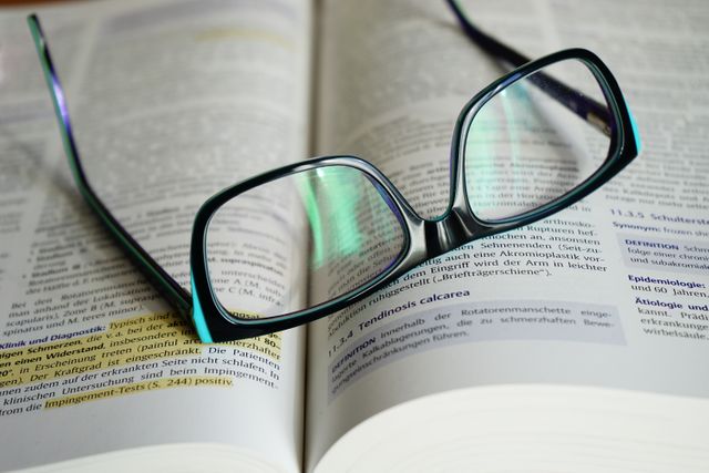 This image shows a close-up of reading glasses resting on an open book with highlighted text. Ideal for representing themes of studying, academic work, or reading. Useful for educational websites, learning blogs, academic presentations, or literature and knowledge-based projects.
