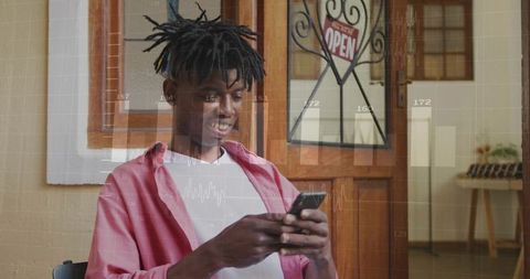 Young man scrolling smartphone at storefront entrance with open sign, casual retail moment