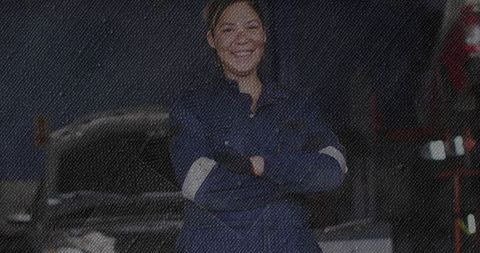 Confident female mechanic in coveralls stands in industrial workshop