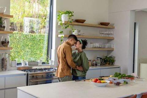 Couple sharing intimate morning moment in modern kitchen with greenery and meal prep