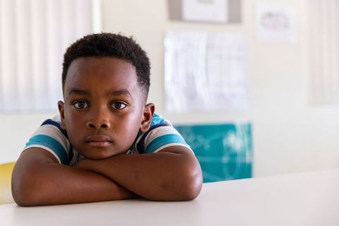 African american boy resting on desk in classroom looking thoughtful and focused