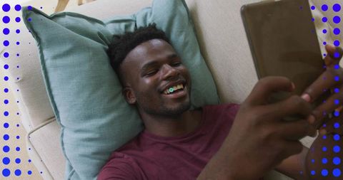 Smiling man relaxing on sofa using tablet for streaming, browsing, and video chat