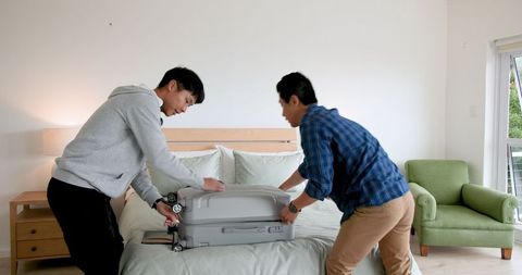 Father and Son Packing for Family Vacation on Bed