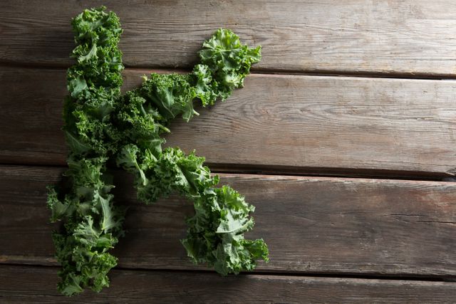 Letter K formed with fresh kale leaves on rustic wooden table. Ideal for healthy eating promotions, organic food campaigns, typography art projects, and nutrition blogs.