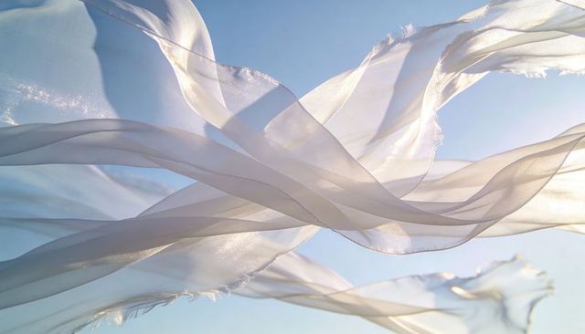 Billowing sheer chiffon layers drifting over pale blue sky with sunlit frayed edges