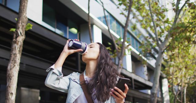 Modern woman enjoying coffee on walk, connecting with phone in urban setting - Download Free Stock Images Pikwizard.com