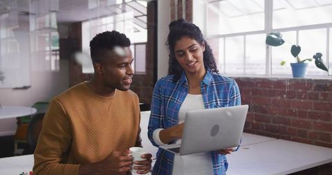 Professionals collaborating over laptop in bright loft office with exposed brick and plants