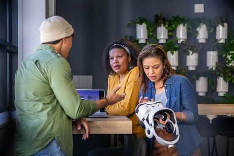 Diverse coworkers collaborating and testing vr headset in modern coworking workspace