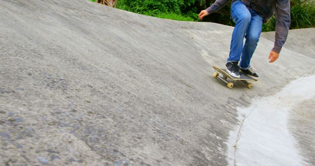 Skateboarder in jeans and casual clothing riding down a concrete slope outdoors, showcasing casual style and passion for extreme sports. Suitable for promotions related to urban lifestyle, skateboarding culture, sports brands, or motivational posters.