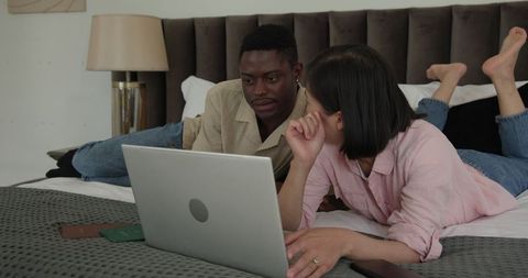 Diverse Team Collaborating on Bed with Laptop and Tablet