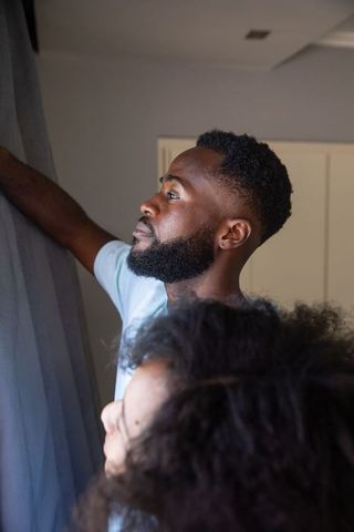 African American Couple Drawing Curtains for Natural Light at Home
