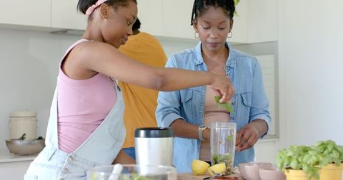 Mother and teen daughter preparing basil smoothie and pesto in bright modern kitchen