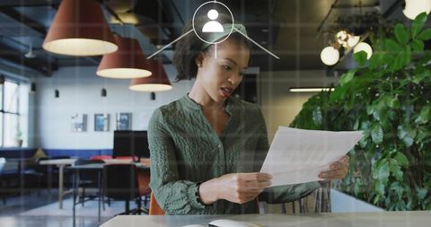 Businesswoman reviewing documents in modern coworking office with digital network overlay