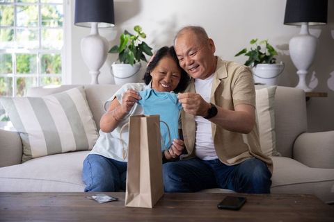 Senior couple receiving baby onesie gift celebrating grandparent announcement at home