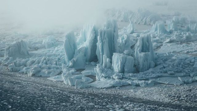 Towering arctic ice spires rising from fractured polar shoreline in misty fog