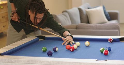 Player leaning over blue-felt pool table lining up precise cue shot in cozy lounge