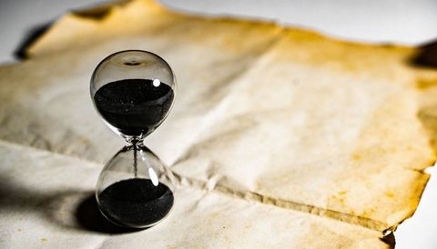 Black sand hourglass on aged parchment conveying time, memory, antique texture and warm light