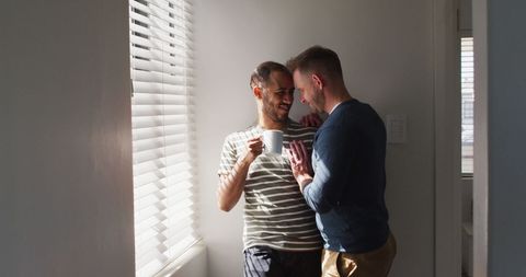 Interracial male couple enjoying coffee and embrace at home