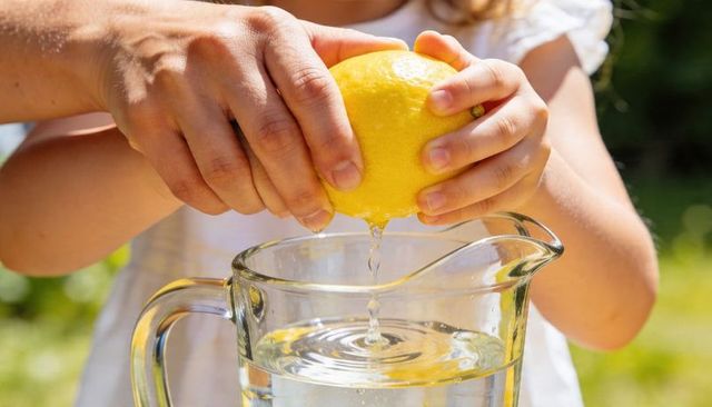 Parent guiding child squeezing lemon into pitcher outdoors on sunny garden afternoon