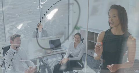 Businesswoman presenting on glass whiteboard while team collaborates in office meeting