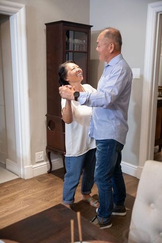 Mature chinese couple dancing at home sharing joyful, intimate moment on hardwood floor