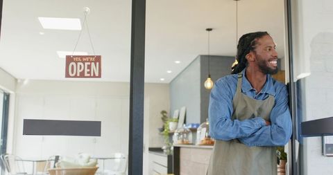 Smiling barista standing at open cafe doorway welcoming customers in modern bakery