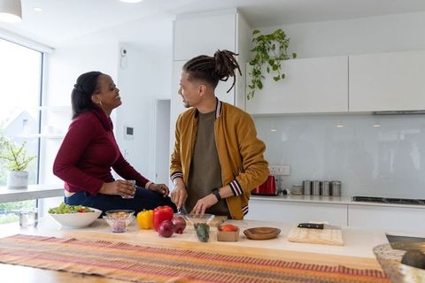 African American couple cooking together at sunlit modern kitchen island, chopping vegetables