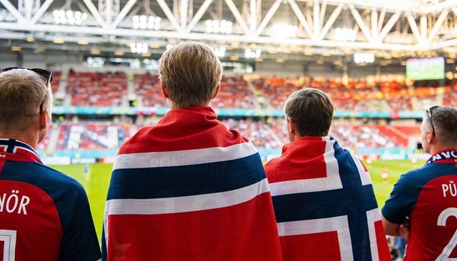 Norwegian football fans watching match draped in national flag at stadium stand