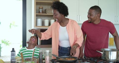 African american family cooking together in bright kitchen, mother playfully feeding child