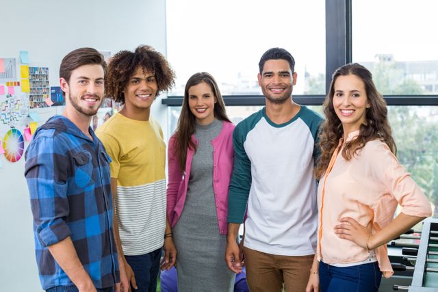 Diverse group of young graphic designers standing together and smiling in a modern office. Ideal for use in articles or advertisements about teamwork, creative industries, modern workplaces, and professional collaboration. Suitable for promoting diversity and inclusion in the workplace.