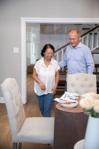 Asian senior couple walking through dining room, man placing hand on woman, warm family moment