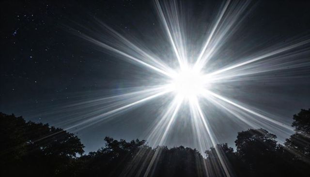 Radiating starburst light casting dramatic rays across night sky over silhouetted trees