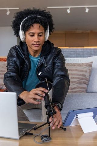African american podcaster adjusting usb microphone in living room studio