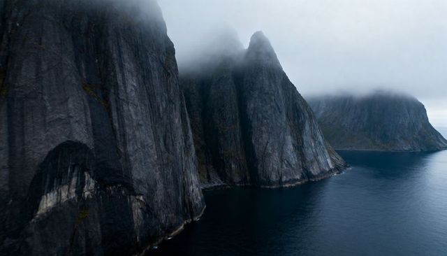Plunging mist-shrouded sea cliffs meeting dark coastal waters at rugged headland