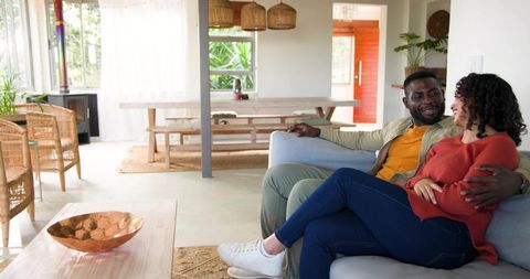 Couple relaxing on sofa in sunlit boho living room sharing conversation and warm moment
