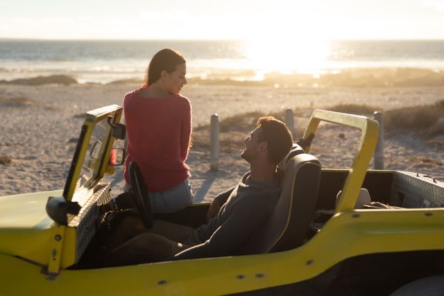 Couple sitting in a beach buggy by the sea during sunset, engaging in conversation. Ideal for use in travel and tourism promotions, romantic getaway advertisements, summer holiday campaigns, and lifestyle blogs focusing on outdoor adventures and road trips.