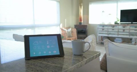 Smart-home tablet showing control dashboard on polished granite countertop with coffee mug
