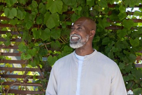 Senior man smiling and looking up in garden wearing beige mandarin collar shirt by trellis