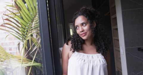African american woman relaxing by sliding glass door in sunlit home