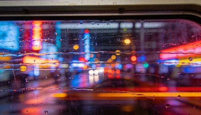 Rain-streaked window capturing neon city bokeh from car interior at night