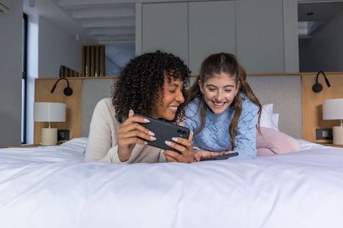 Diverse Female Friends Relaxing on Bed Sharing Smartphones