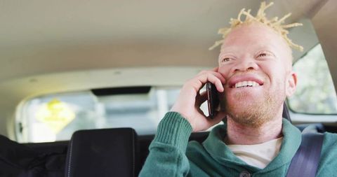 Smiling passenger talking on phone in rear car seat wearing green sweater and seatbelt