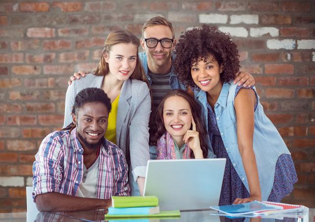 Group of diverse students studying together with a laptop and books, smiling at camera. Perfect for use in educational websites, promoting diversity in classrooms, teamwork in education, or student life marketing materials.