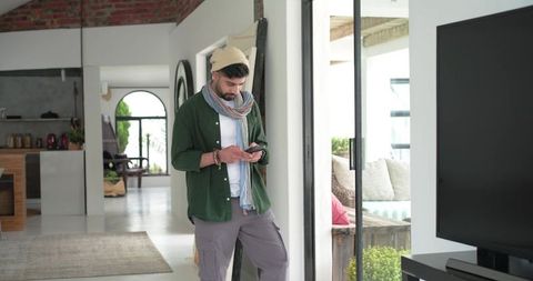 Indian man checking smartphone by sliding glass door in modern open-plan home interior