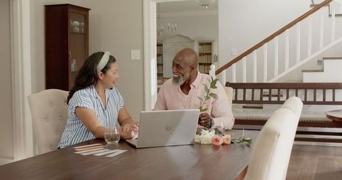 Senior Diverse Couple Planning Celebration with Laptop at Home