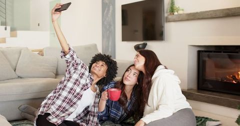 Diverse women relaxing and taking selfie at home indoors