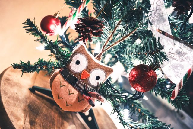 Charming owl ornament hanging on a beautifully decorated Christmas tree with lights and baubles. Perfect for holiday season promotions, festive greeting cards, ecommerce websites selling Christmas decorations, or winter-themed magazine articles.