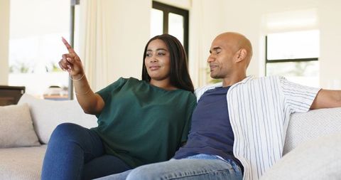 Couple relaxing on sofa pointing right in bright modern living room casual home lifestyle