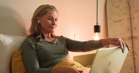 Senior Woman Reclining on Bed Using Laptop for Online Connectivity